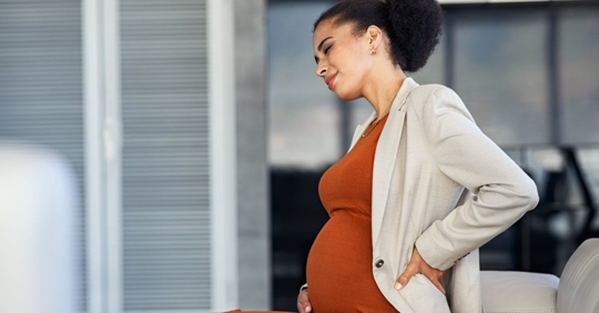Pregnant female employee standing up with her hand on her back