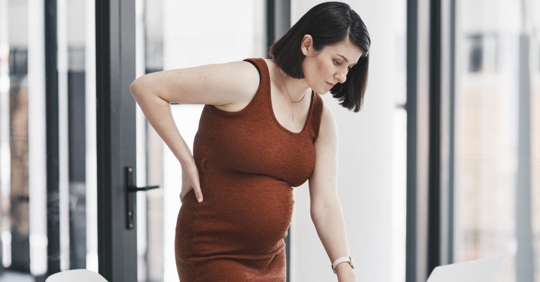 Pregnant female employee standing up with her hand on her back