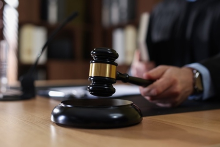Judge striking gavel at wooden table indoors, selective focus